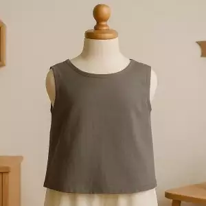 A smoky gray organic muslin baby top with a stylish cross-back design, perfect for warm weather, displayed on a mannequin in a cozy nursery with natural light.