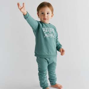 Toddler boy wearing a cozy natural green organic cotton sweatshirt and sweatpants set with ‘Believe in Magic’ print. Comfortable unisex fall outfit perfect for everyday play or as a baby shower gift.